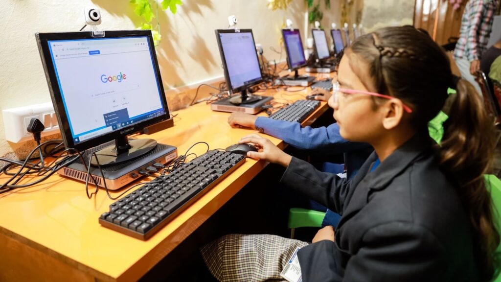 A girl using a computer in a classroom setting with other students, promoting digital learning and technology education