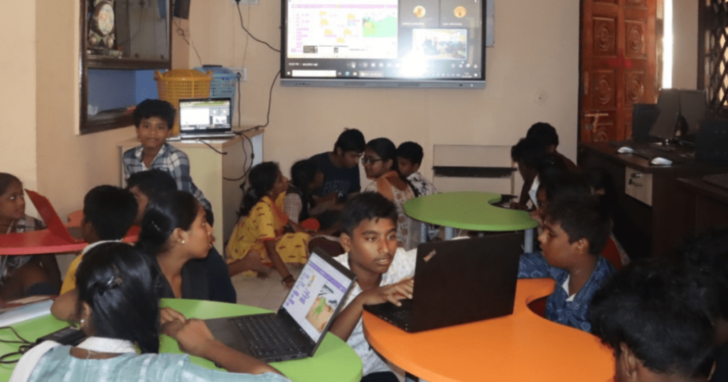 Students in an ApniPathshala computer lab, following a digital curriculum with an instructor, focused on screens in a structured learning pod.